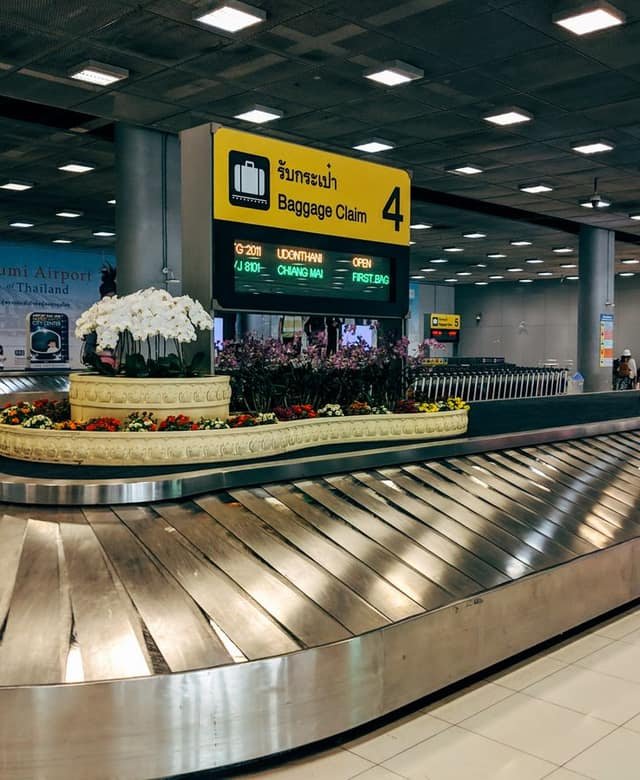 An empty stainless-steel baggage-claim carousel curving around a display of orchids, a yellow overhead sign reading Baggage Claim 4.
