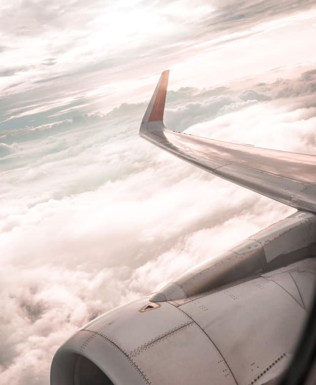 The wing of an airliner catching warm light above a thick blanket of clouds at sunset, the engine cowling in the foreground.