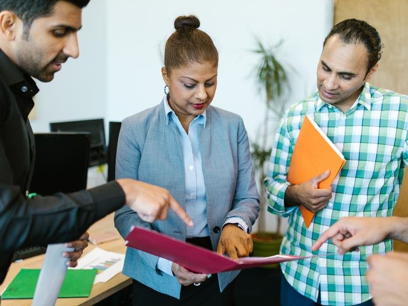 Three South Asian colleagues around a desk going through the papers in an open folder together